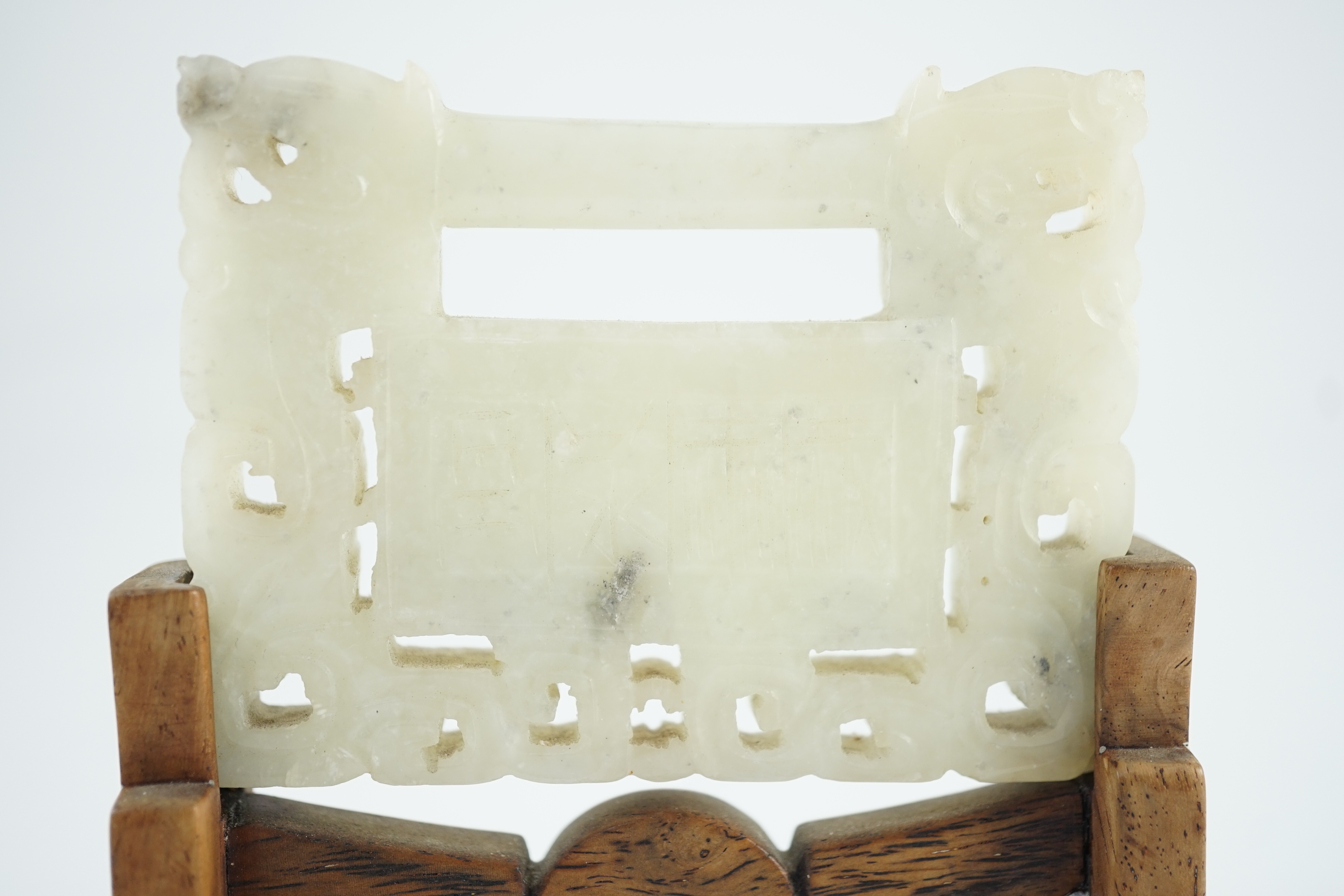 A Chinese speckled white jade ‘lock’ pendant plaque, 19th/20th century, 7.6cm x 5.8cm, wood stand